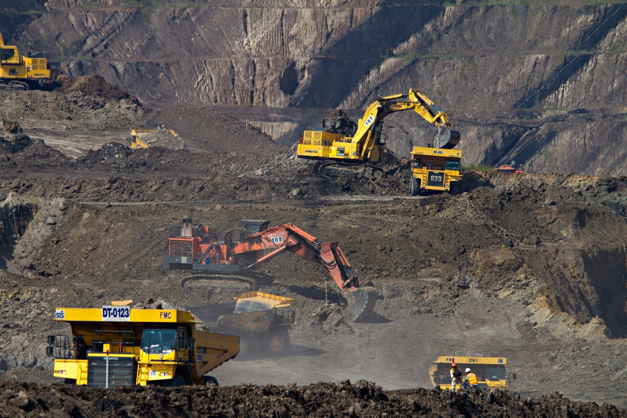 Excavators and haul trucks operate in a nickel mine in South Kalimantan, Indonesia, in 2018, moving earth across terraced excavation pits.