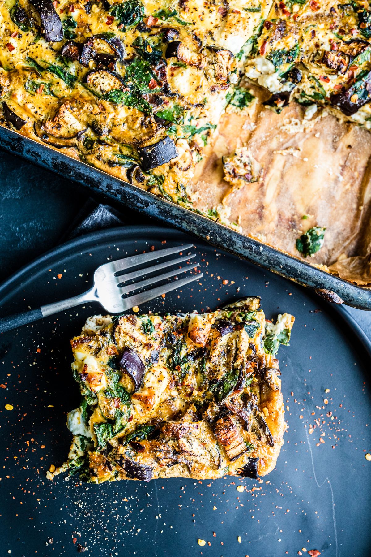 One piece of frittata from a tray, on a black plate with a fork