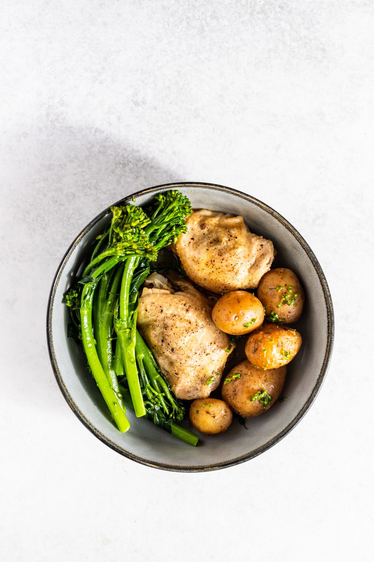 One pot slow cooked chicken thighs potato and broccoli in a bowl on a white background