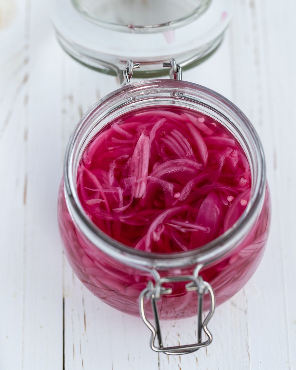 Quick pickled red onions in a glass jar on a white background