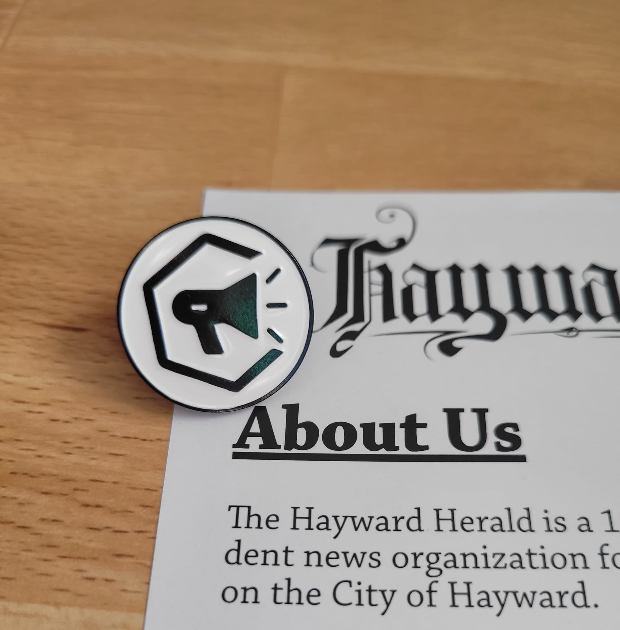 Photo of a Hayward Herald lapel pin next to a page of a zine.