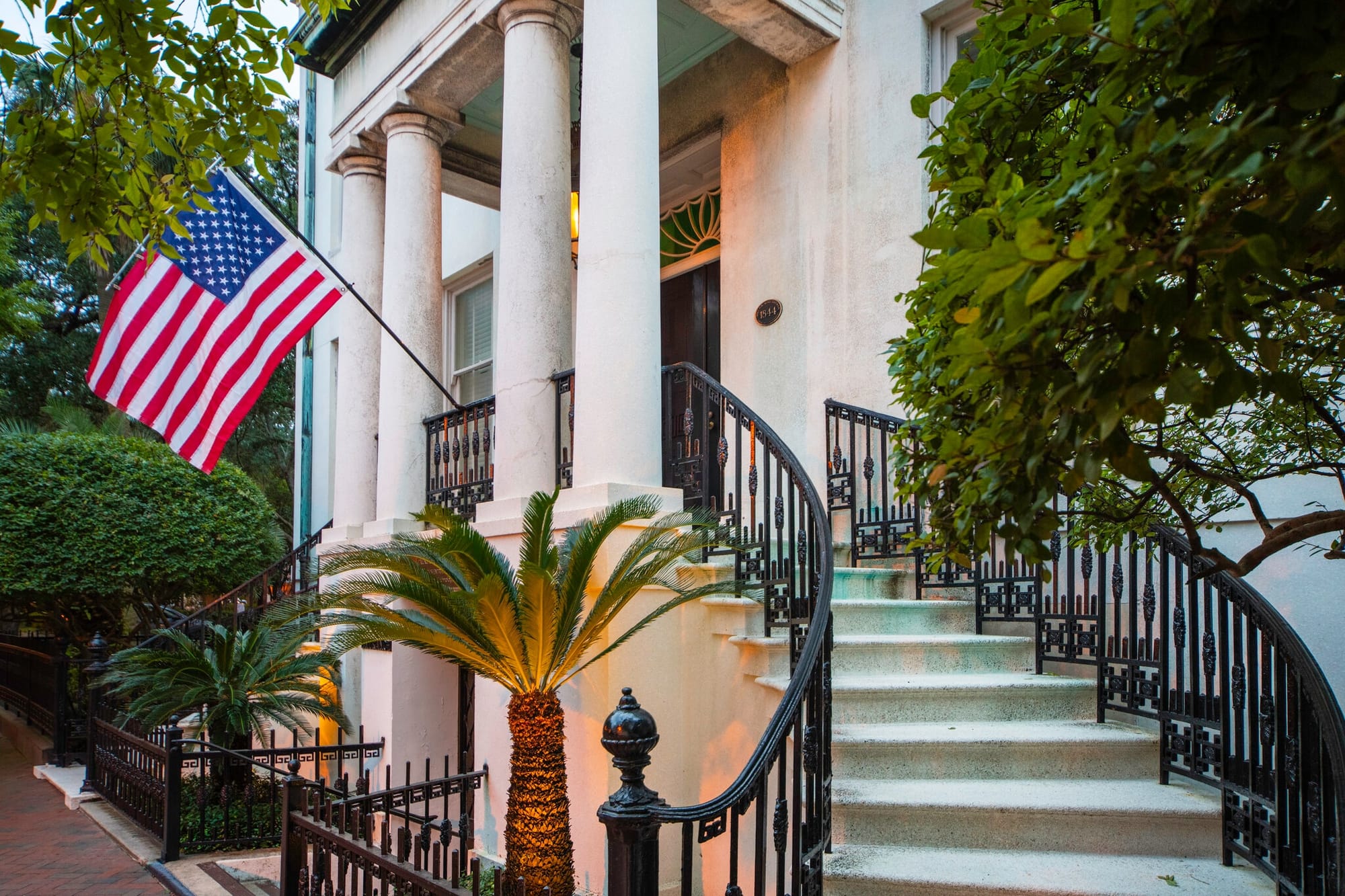 An American flag is displayed in front of a columned entrance to a Greek Revival-style city mansion.