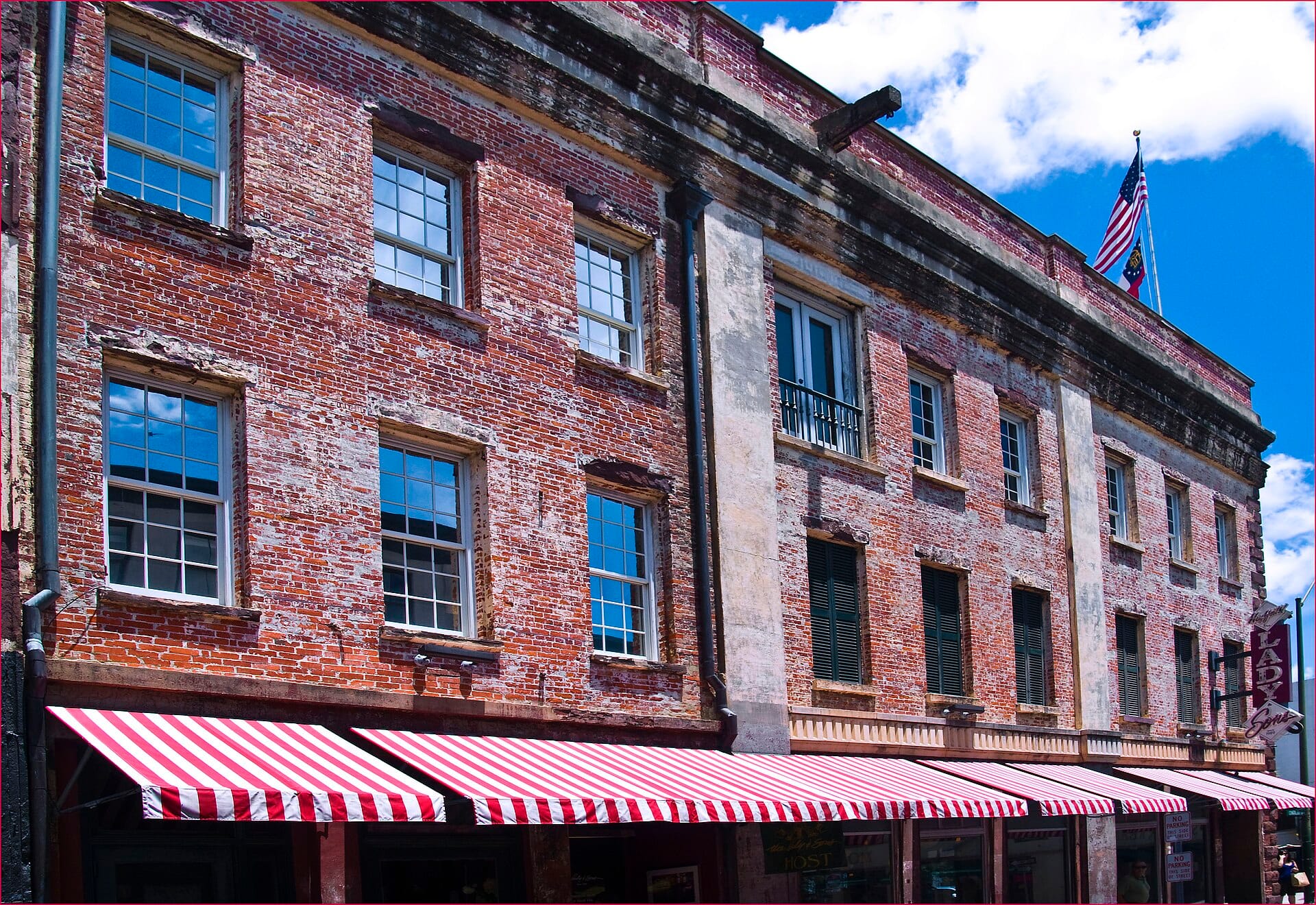 A historical brickfront building with red and white striped awning, against a blue sky.