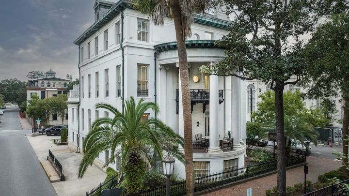 A white mansion with columns and large palm trees in front.