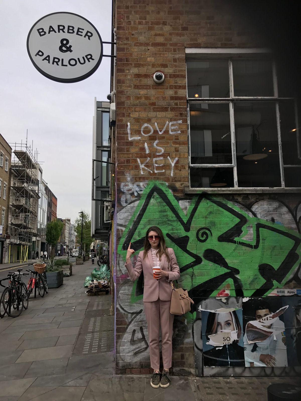 A woman in a pink suit points towards graffiti that says ‘love is key’