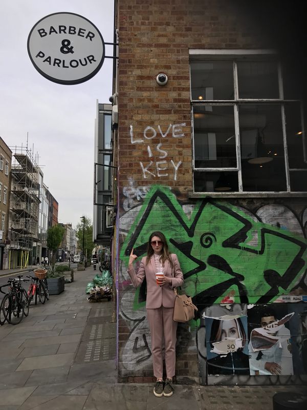 A woman in a pink suit points towards graffiti that says ‘love is key’