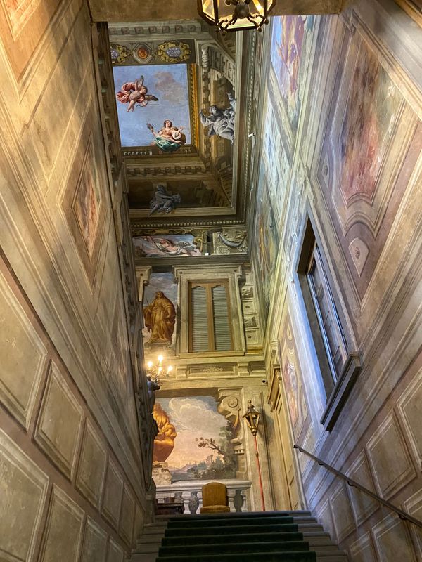 A grand carpeted staircases with colourful frescoes on the walls.