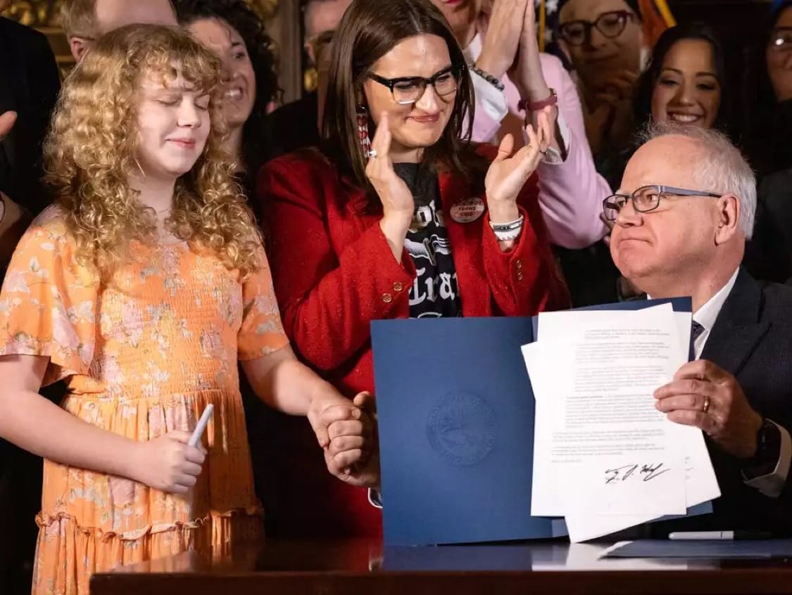 Governor Tim Walz shaking hands with 12-year-old Hildie Edwards, who is undergoing sex reassignment. In his other hand, he holds the bill he signed, making Minnesota a refuge for those seeking to transition their children. Photo: @aleclace/X