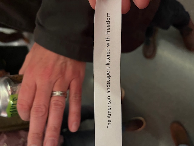 A small piece of paper that says The American landscape is littered with freedom, with a hand behind it.