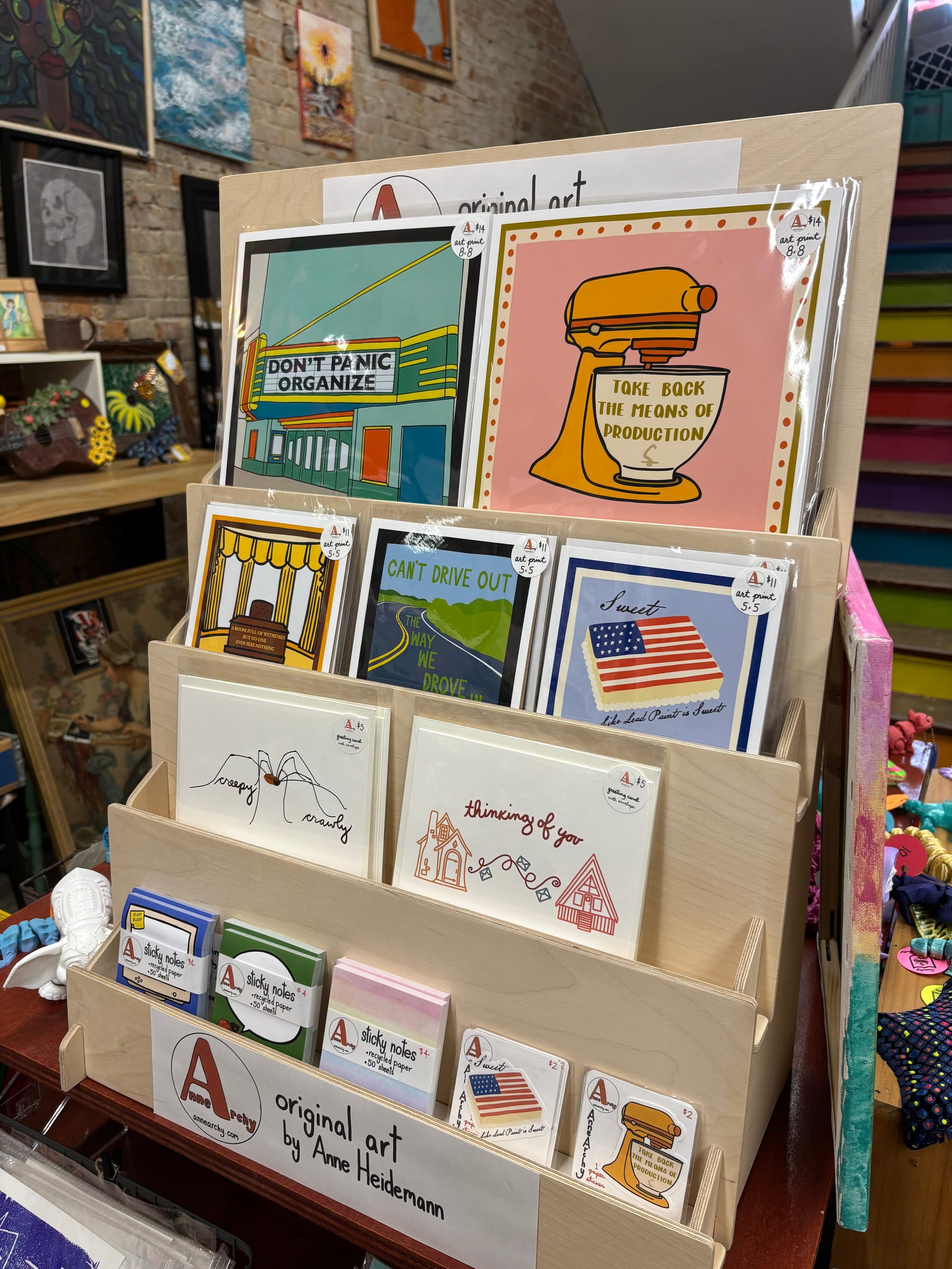a display of art and wares by AnneArchy, including art prints, blank-inside cards, sticky notes, and stickers