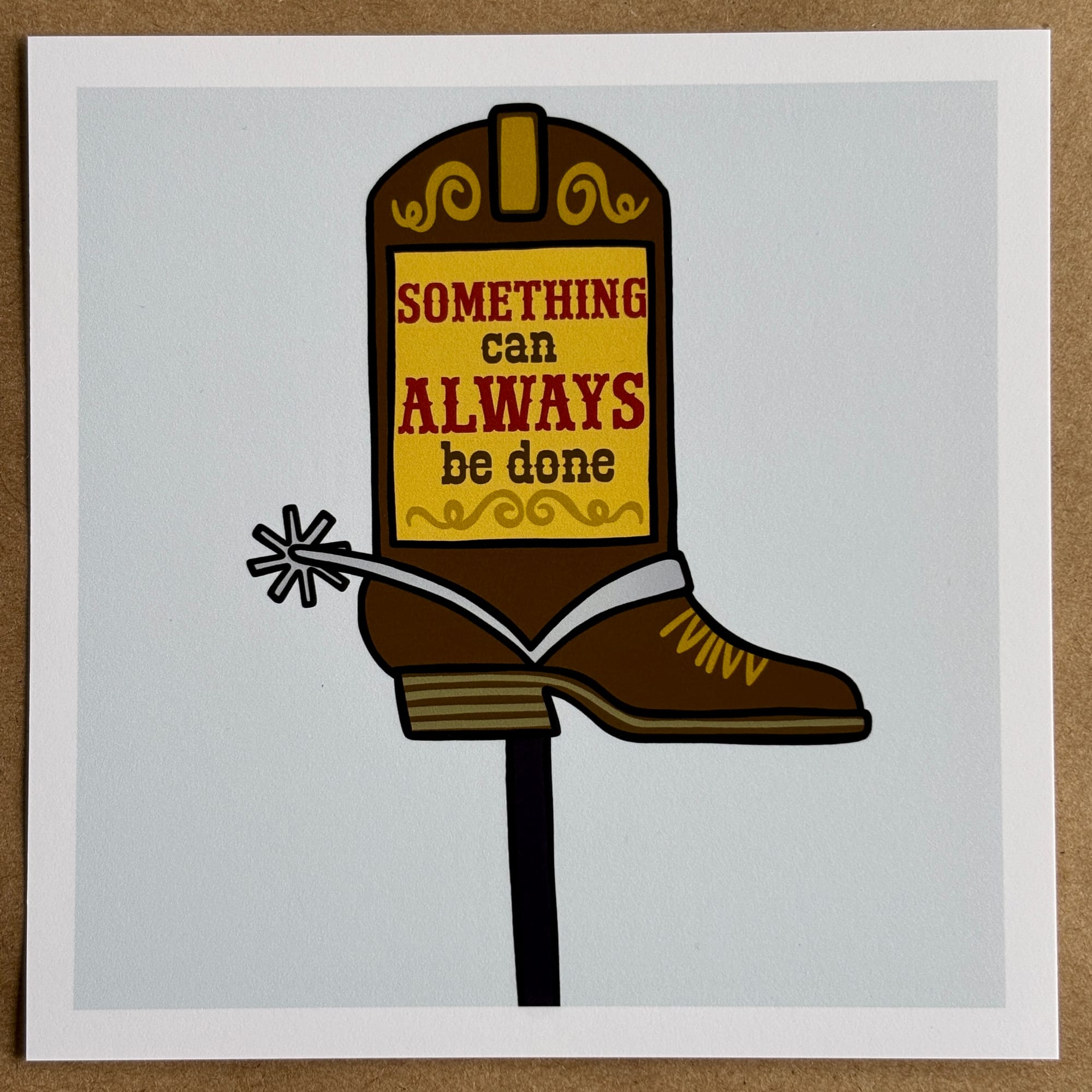 Original art by AnneArchy of a sign in the shape of a cowboy boot with hand-lettering of the words "something can always be done." 