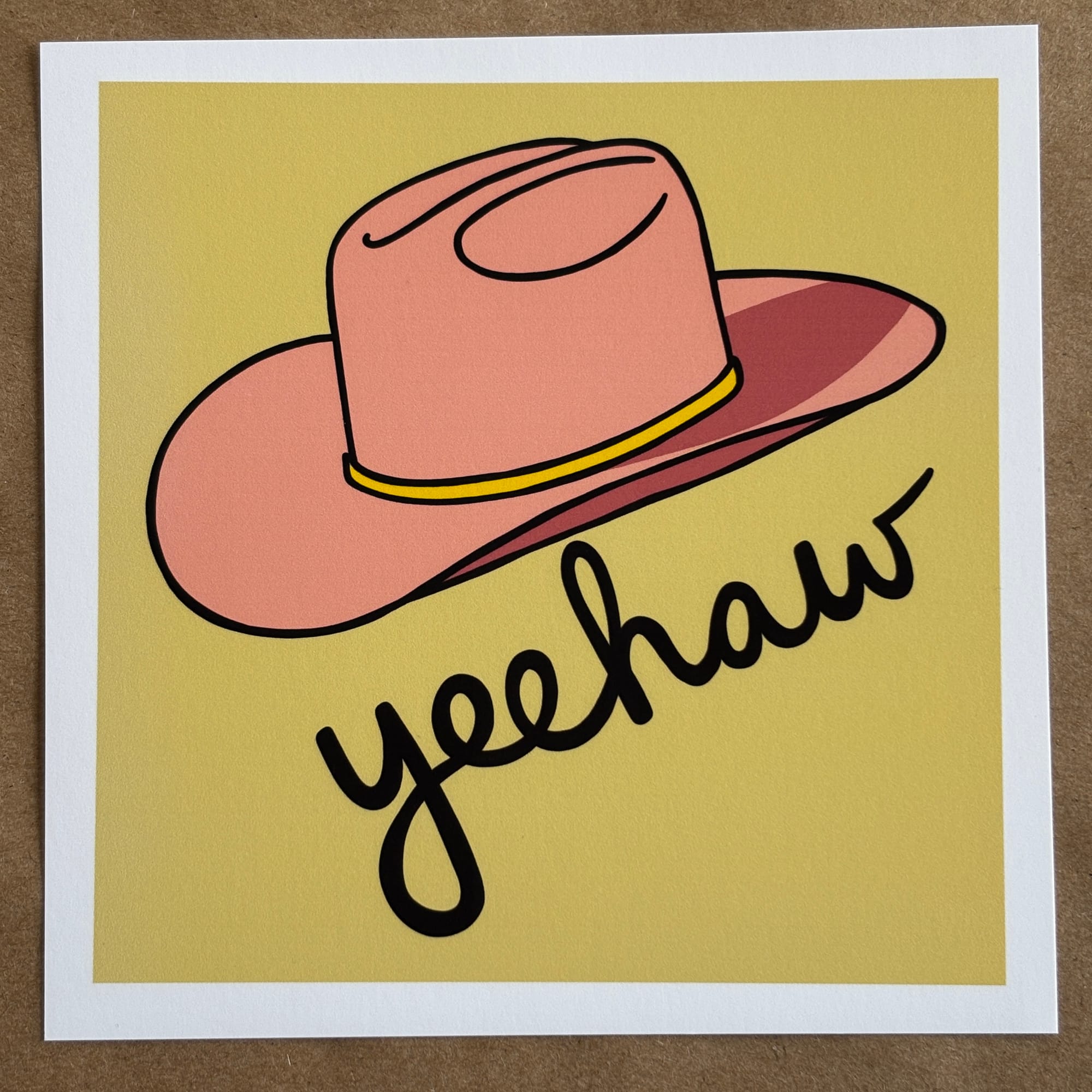 original art by AnneArchy of a pink cowboy hat with hand-lettering of the word "yeehaw.”