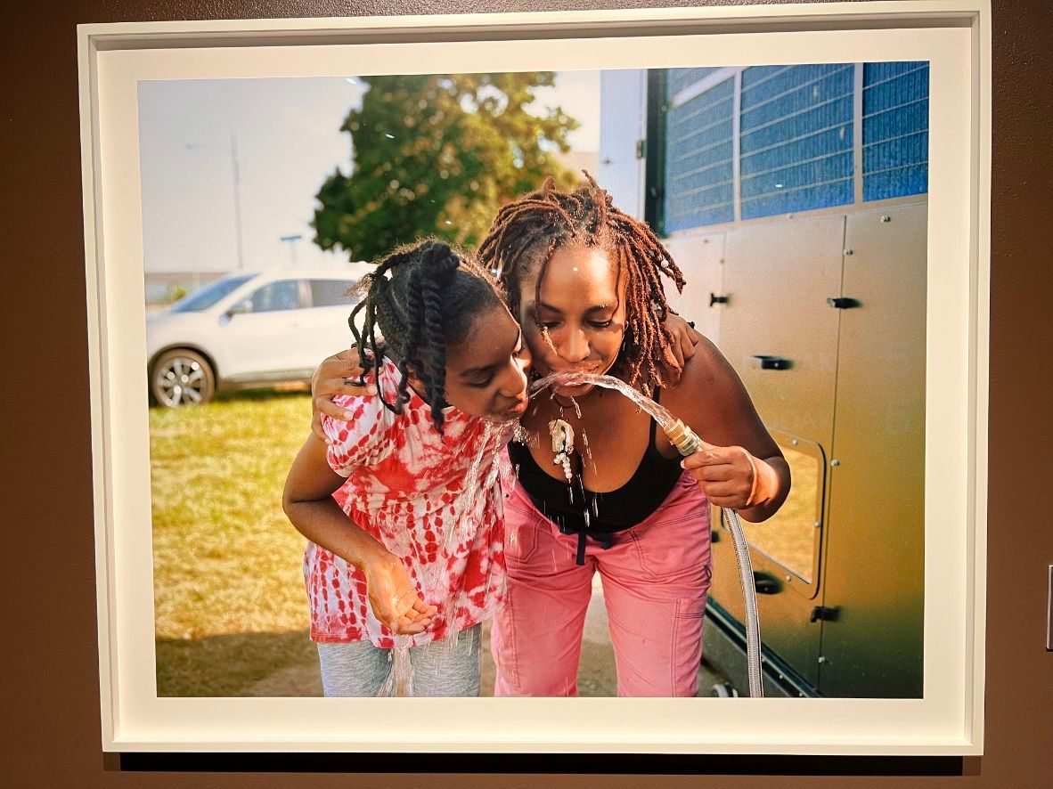 Image-of-a-photograph,-a-woman-and-young-girl-drink-water-from-a-hose
