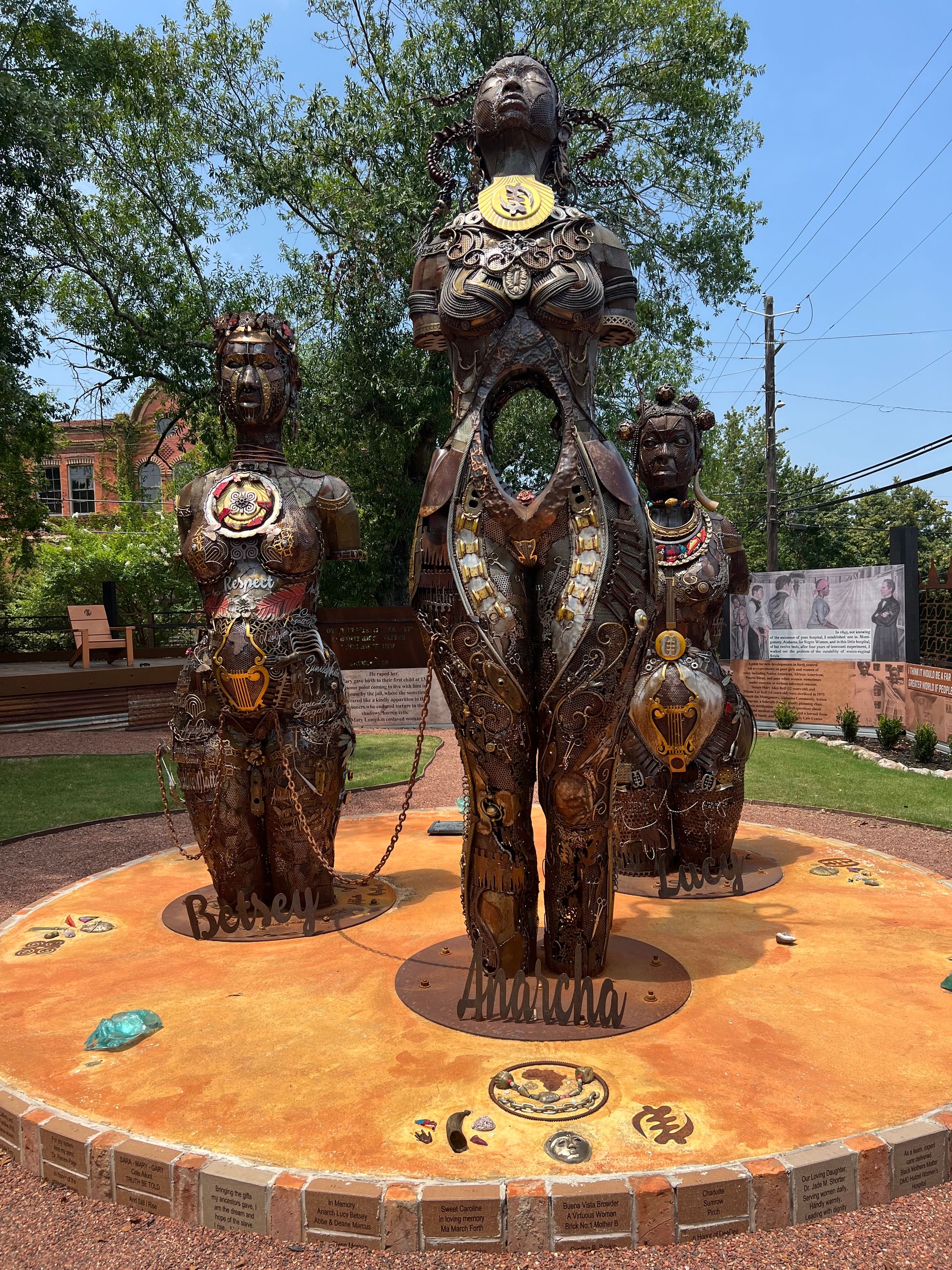Three bronze statues made of scrap metal and covered in things like scissors, jewels, words naming influential Black women