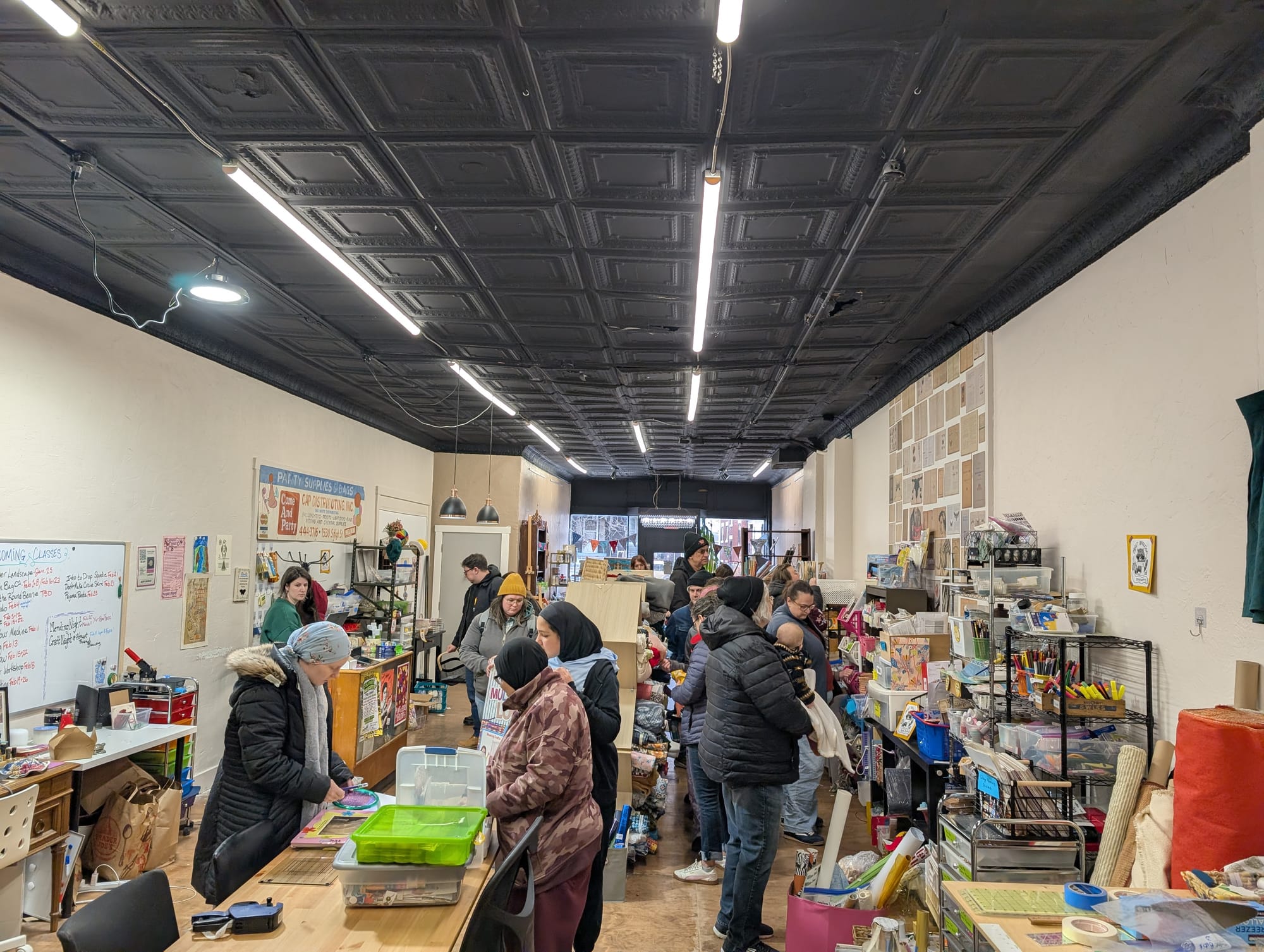 A small crowd of people walk through a store filled with tables, shelves, and miscellaneous items