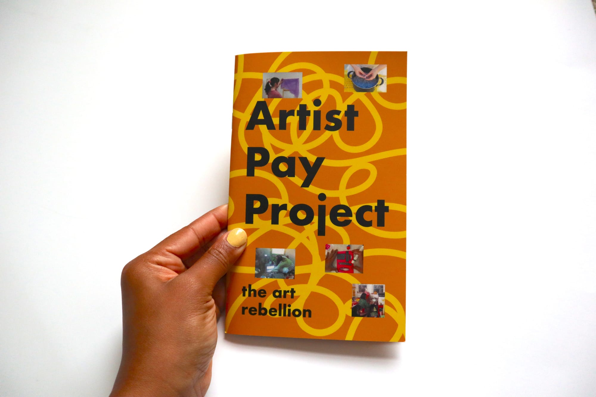 Close up photo of a yellow and orange zine that reads "Artist Pay project" and a hand holding it.