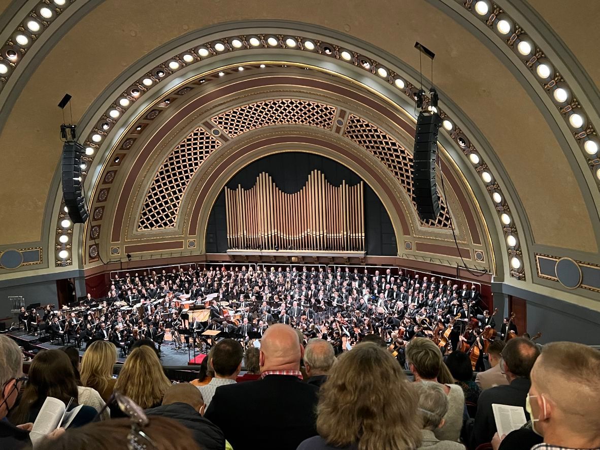 Inside-a-performance-hall,-an-audience-claps-for-a-stage-filled-with-musicians.