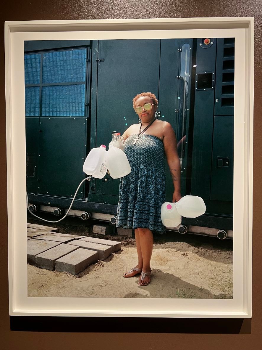 A-woman-in-a-blue-dress-and-flats-holds-several-water-jugs
