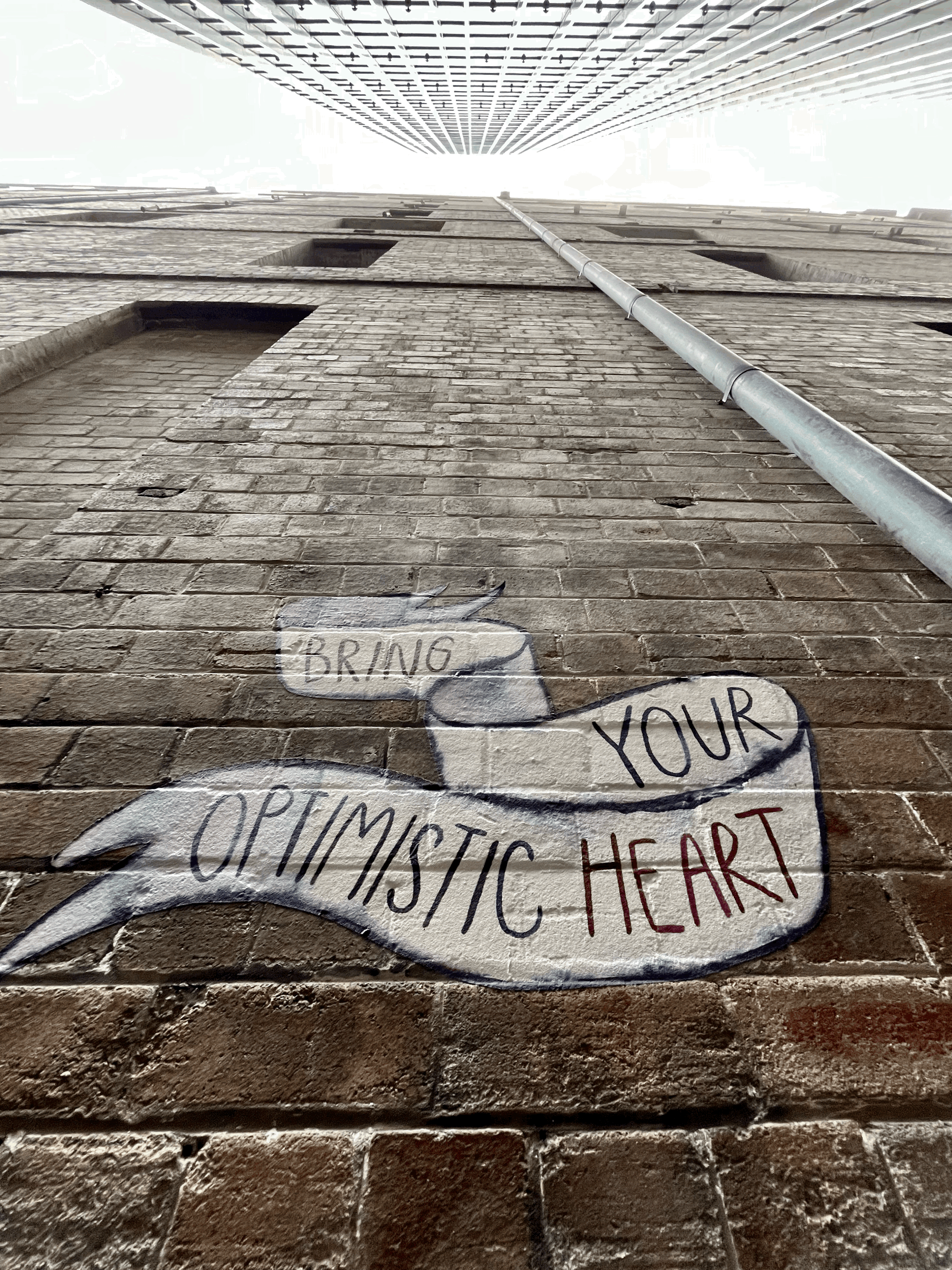 A piece of alleyway artwork near Bridge Street in the Sydney CBD, Australia. It's a painted message that says "Bring Your Optimistic Heart" on brick. Photo by Me.