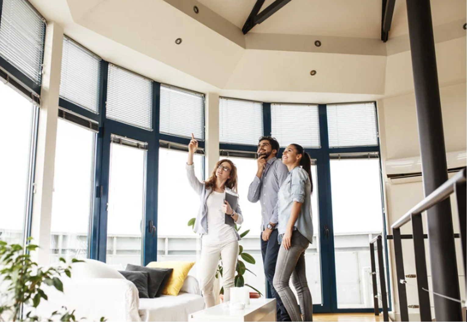 Real estate agent showing luxury condo to young couple in a modern living room with large windows and open layout. 