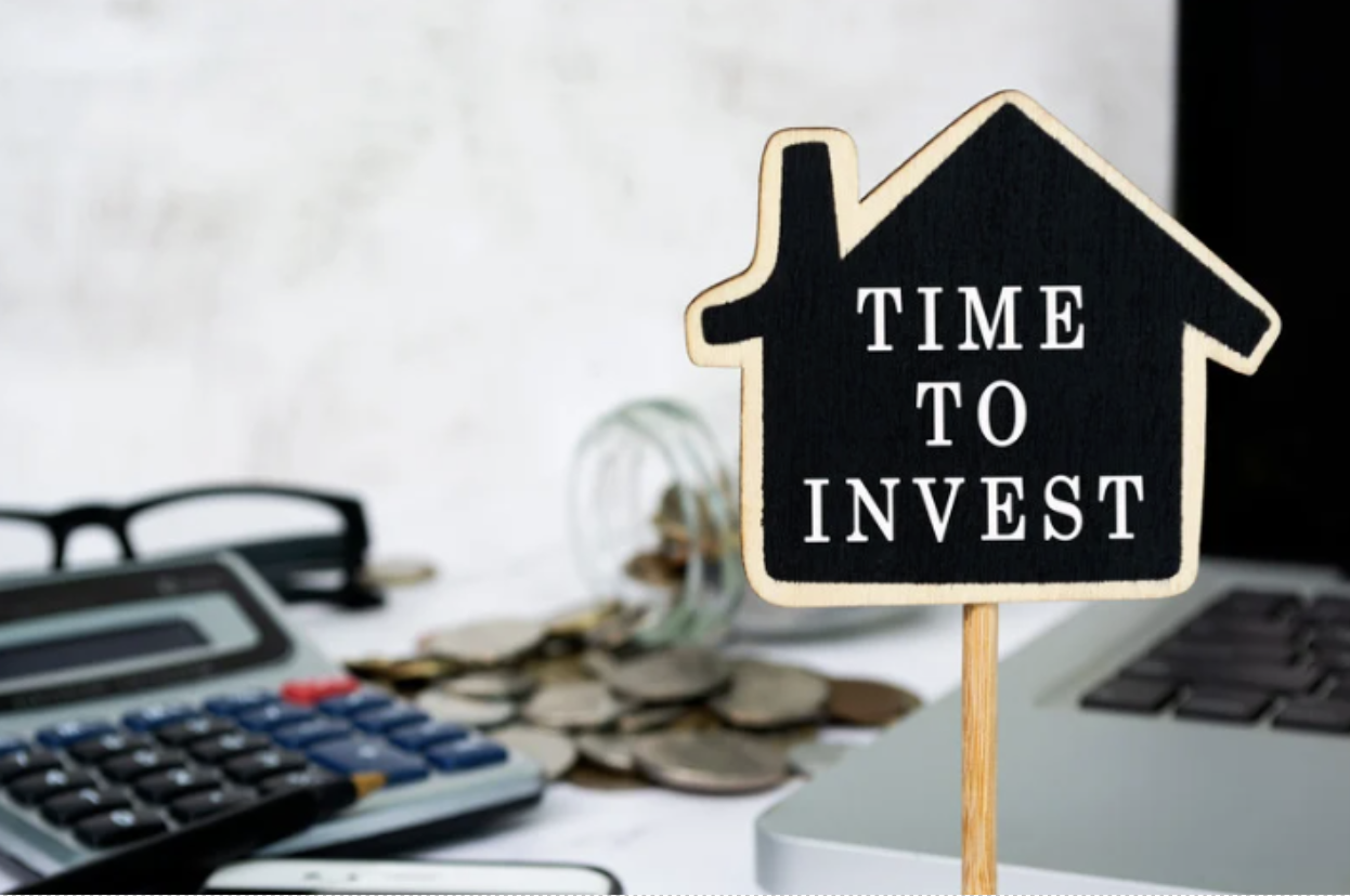 Investment concept with house-shaped sign reading Time to Invest beside calculator and coins. 