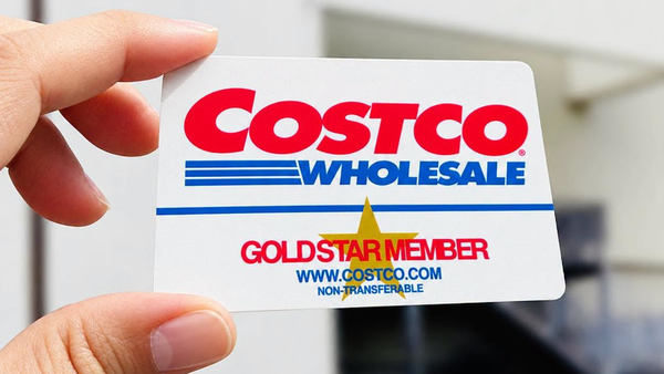 手持好市多 Costco 會員卡，背景為倉儲店外牆招牌。