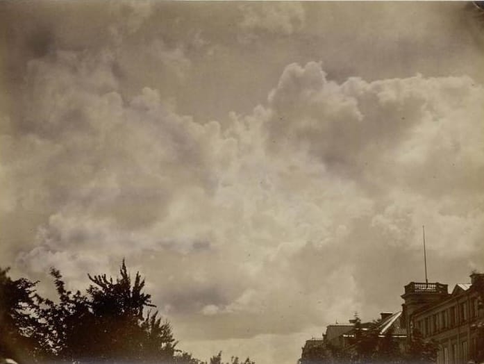 Sepia-toned photograph showing complex cottony cloud formations over barely-visible trees and 19th century architecture.