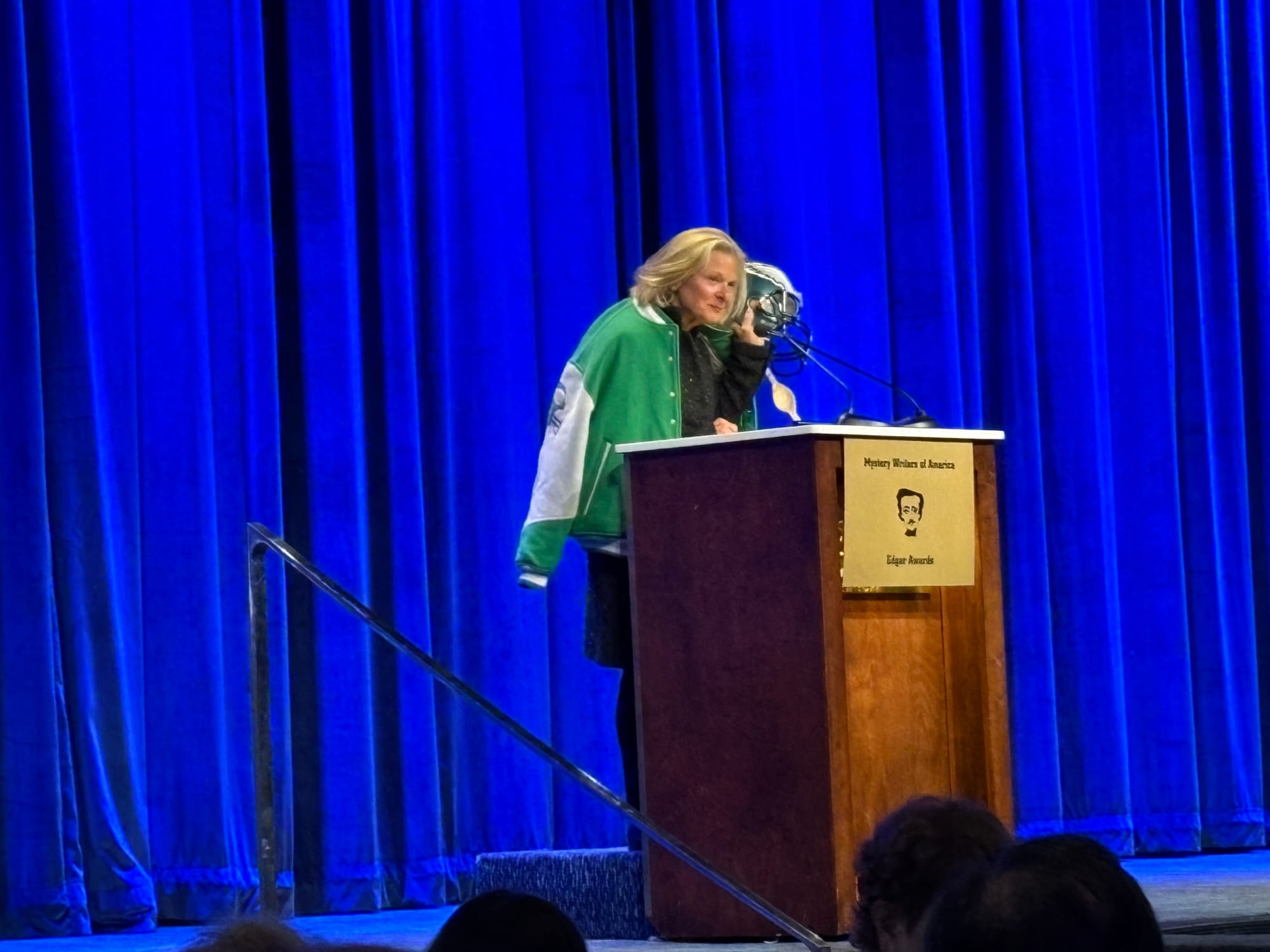 Woman on stage behind podium, holding up a helmet. 