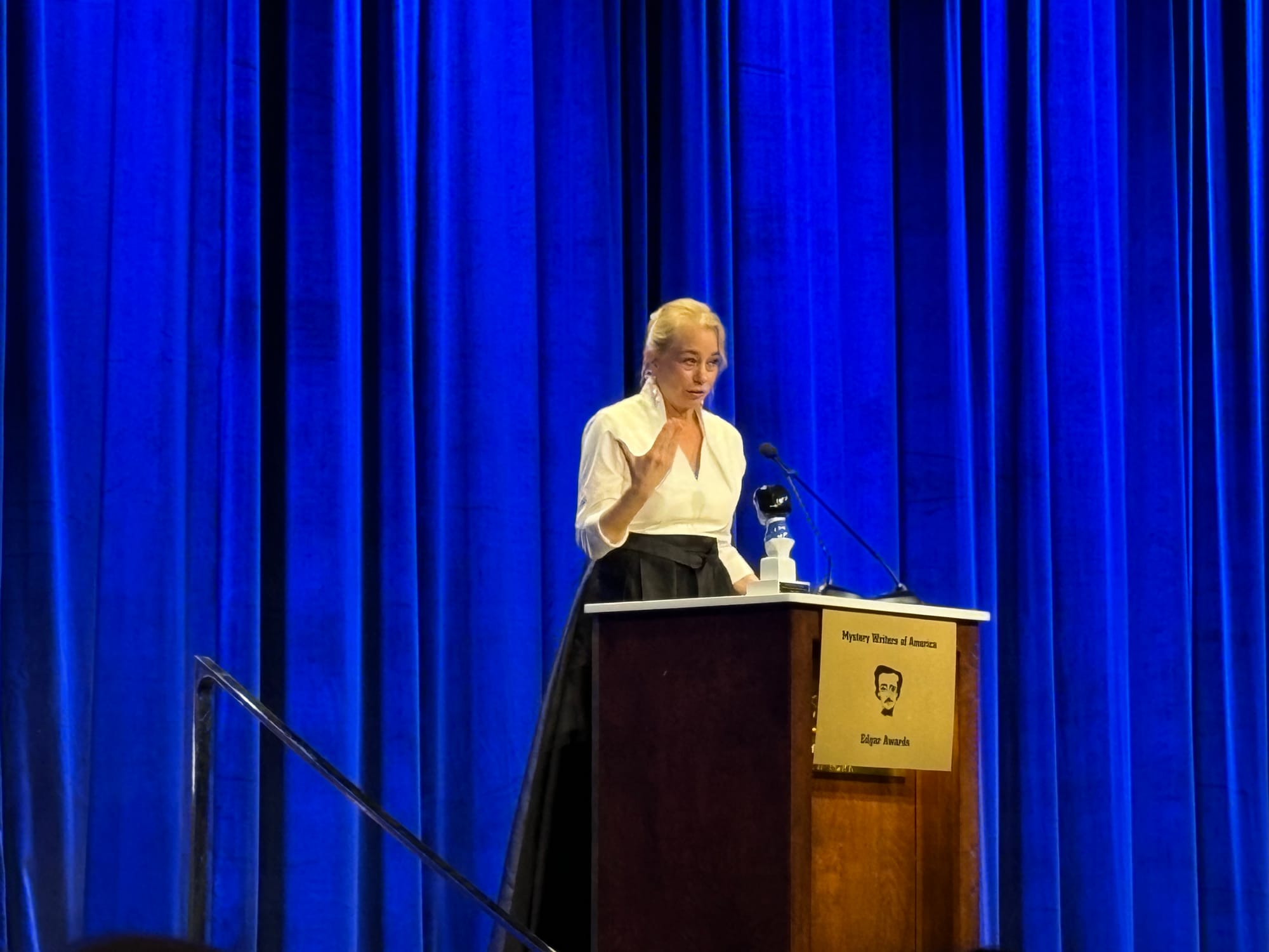 Woman on stage behind podium, holding Edgar Allan Poe bust. 