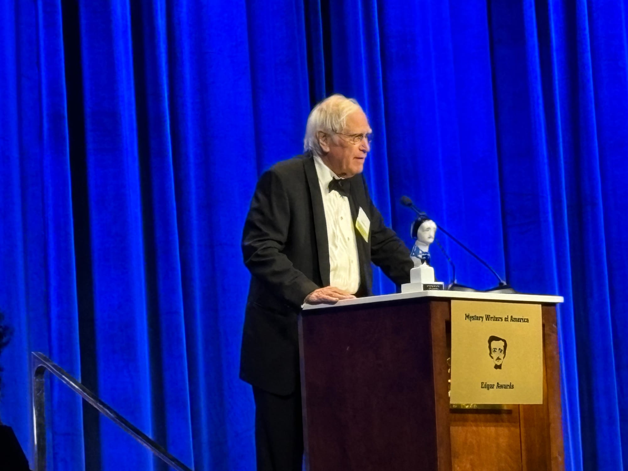 Man at podium, holding bust of Edgar Allan Poe
