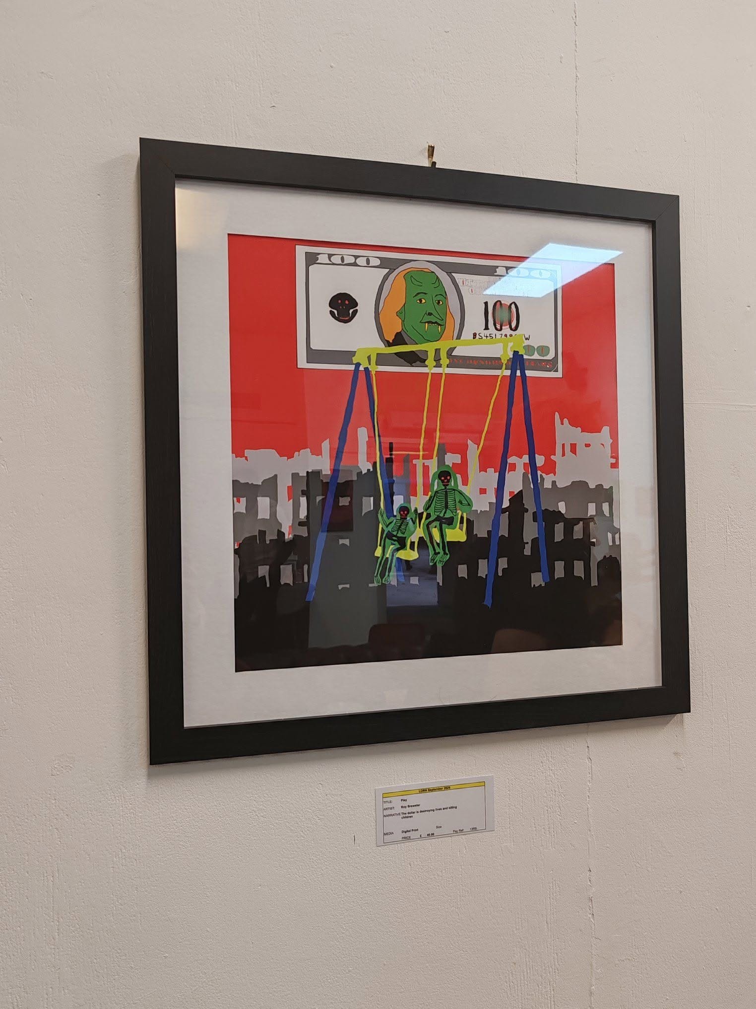 a square black framed artwork hangs on a white wall. In the artowkr two skeletons are swinging side by side against a silhouette city scape in black grey and red. Above the city a stylised 100 dollar bill with the face of the president depicted as a green monster.