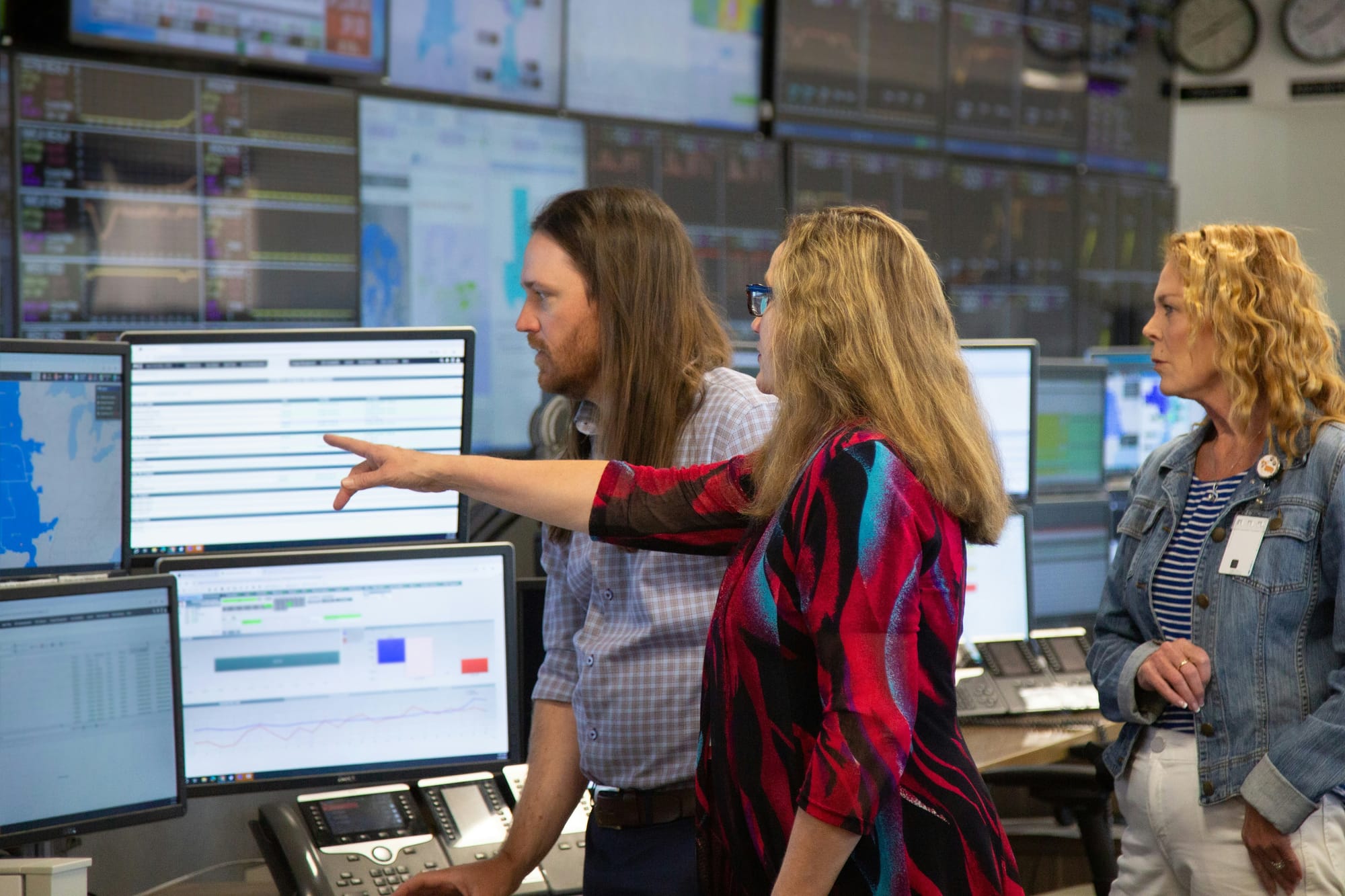 Two women and a man look at monitors in a room full of computers