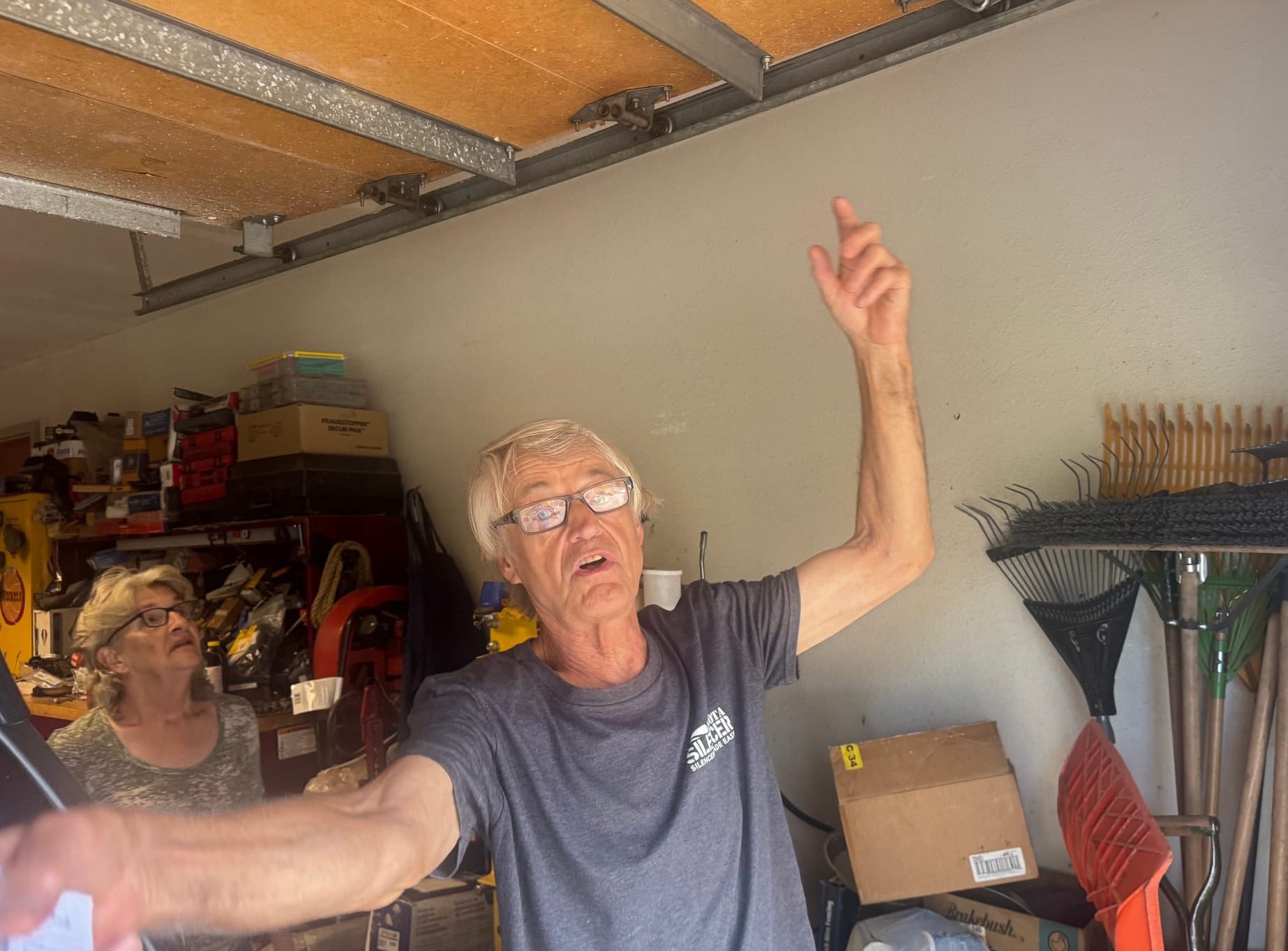 Darrell Koepp of Black Hawk, S.D., with wife Jennifer to the left, demonstrates how vibrations from large explosions at a limestone mine adjacent to their home has made their garage door opener inoperable