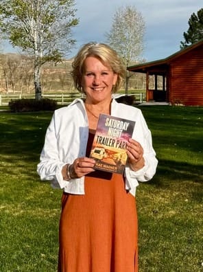 Author Kae Wagner outdoors in Wyoming, smiling and holding Saturday Night at the Trailer Park
