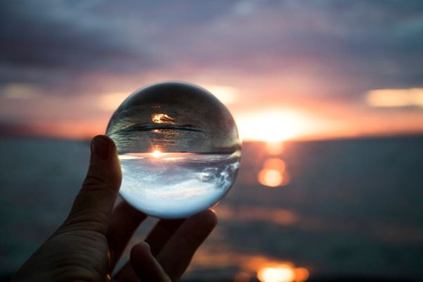 Vivid blue pink orange sunset seascape over ocean, reflected in hand-held glass ball