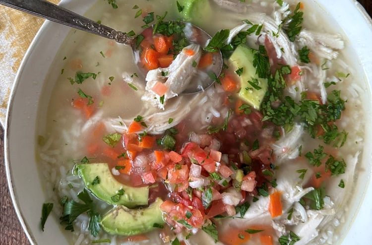 bowl of chicken and rice soup with avocado and pico de gallo