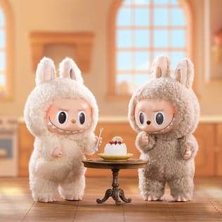 It’s a picture with two li’l monster-lookin fuzzy guys standin at a small wooden table with a cake on it. The monsters have like these li’l bunny ears & big smiles with lotsa pointy teeth pokin out. They’re cute but also they look kinda devious, like maybe they’re gonna get up to some kinda mischief.