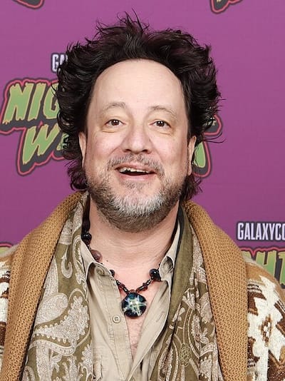 A guy with kinda crazy hair and a button-up with the top coupla buttons unbuttoned & some kinda new-agey-seemin pendant hangin ’round his neck.