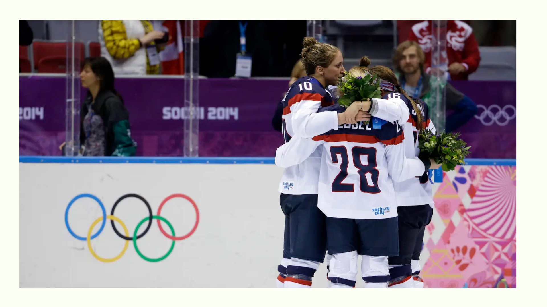 Women's ice hockey team huddling with bouquets at the Sochi 2014 Winter Olympics, Olympic rings visible on the rink.