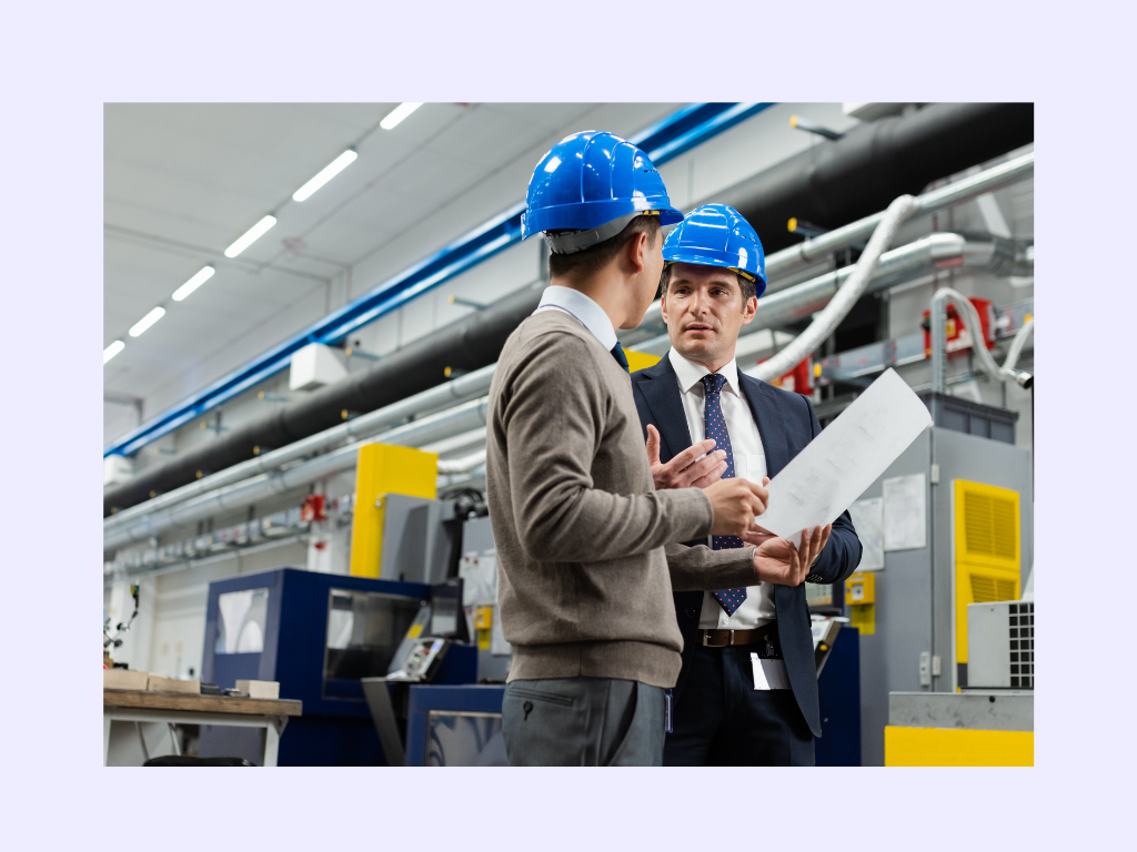 Two engineers in hard hats discussing a document in a modern industrial setting, symbolizing collaboration and decision-making