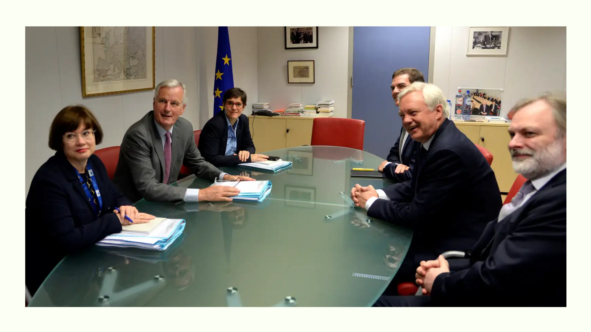 Group of officials seated around a conference table, with documents and an EU flag in the background, discussing a meeting agenda.