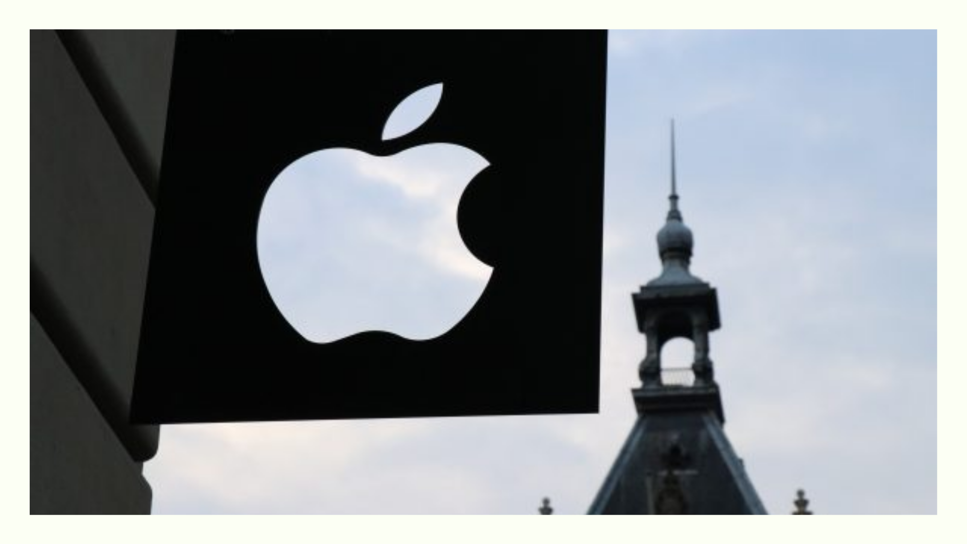 Apple logo on a storefront sign with a historic building and tower in the background, representing an Apple store location.
