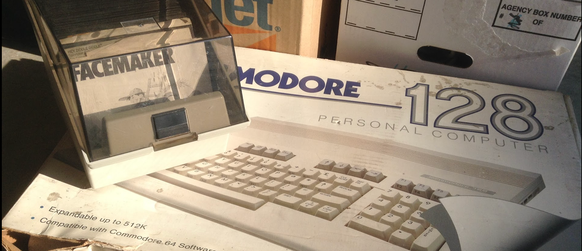 A photograph of a Commodore 128 original box. A container of floppy disks sits on top of it with a disk labeled "Facemaker" in the front.