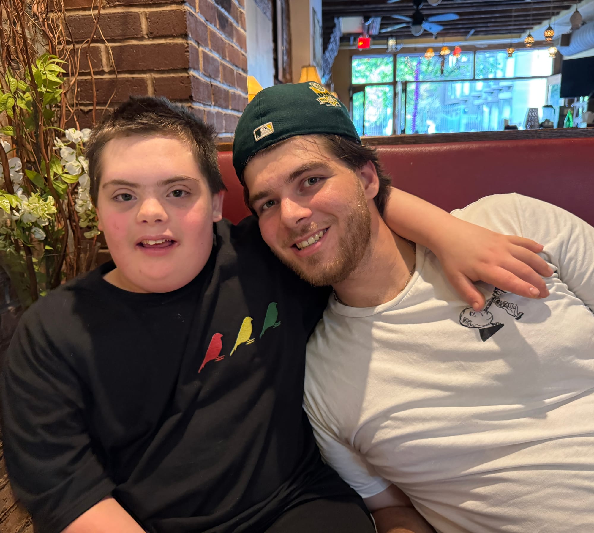 Two brothers sitting in a restaurant booth embracing