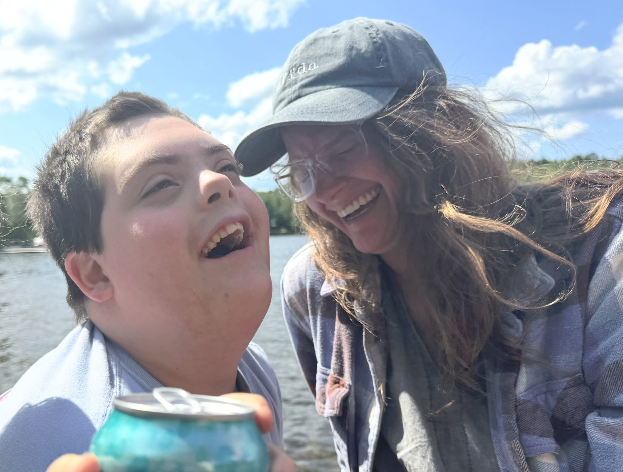 A teen boy and his mother laughing together next to a body of water