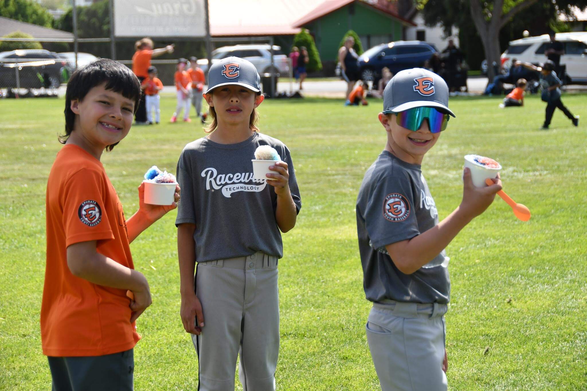 Three players hydrate with snow cones in the spring sunshine.