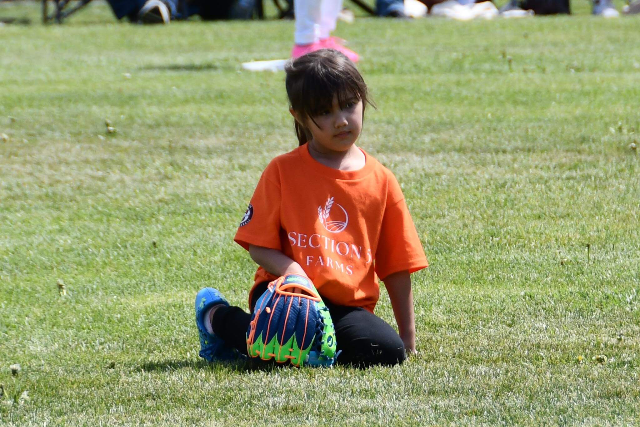 A young outfielder kneels for a break during her T-ball game.