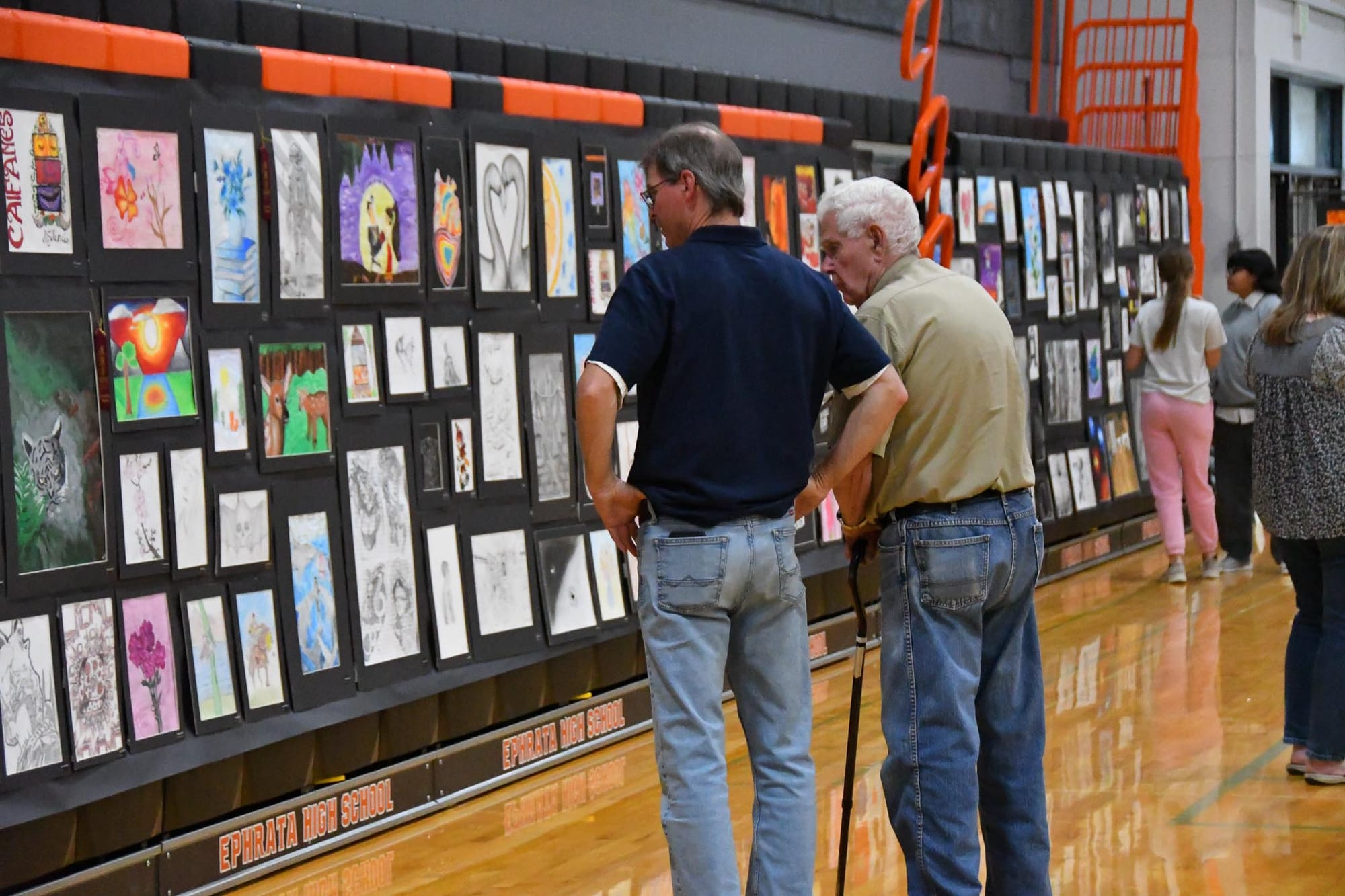 EMS art teacher Brian Forster (left) looks over another wall of student pieces inside the EHS gymnasium.