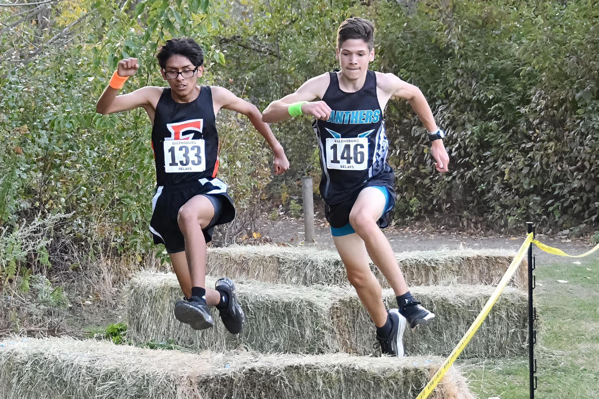 Ephrata's Ryan Delgado and a Bonney Lake runner clear the hay bales side by side Friday at Ellensburg.