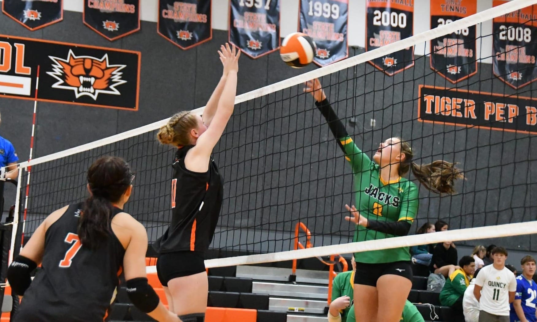 Tiger Bergen Lauver goes up at the net against Quincy's Sadie Stoddard (8) as Addison Vasquez (7) backs up the play.